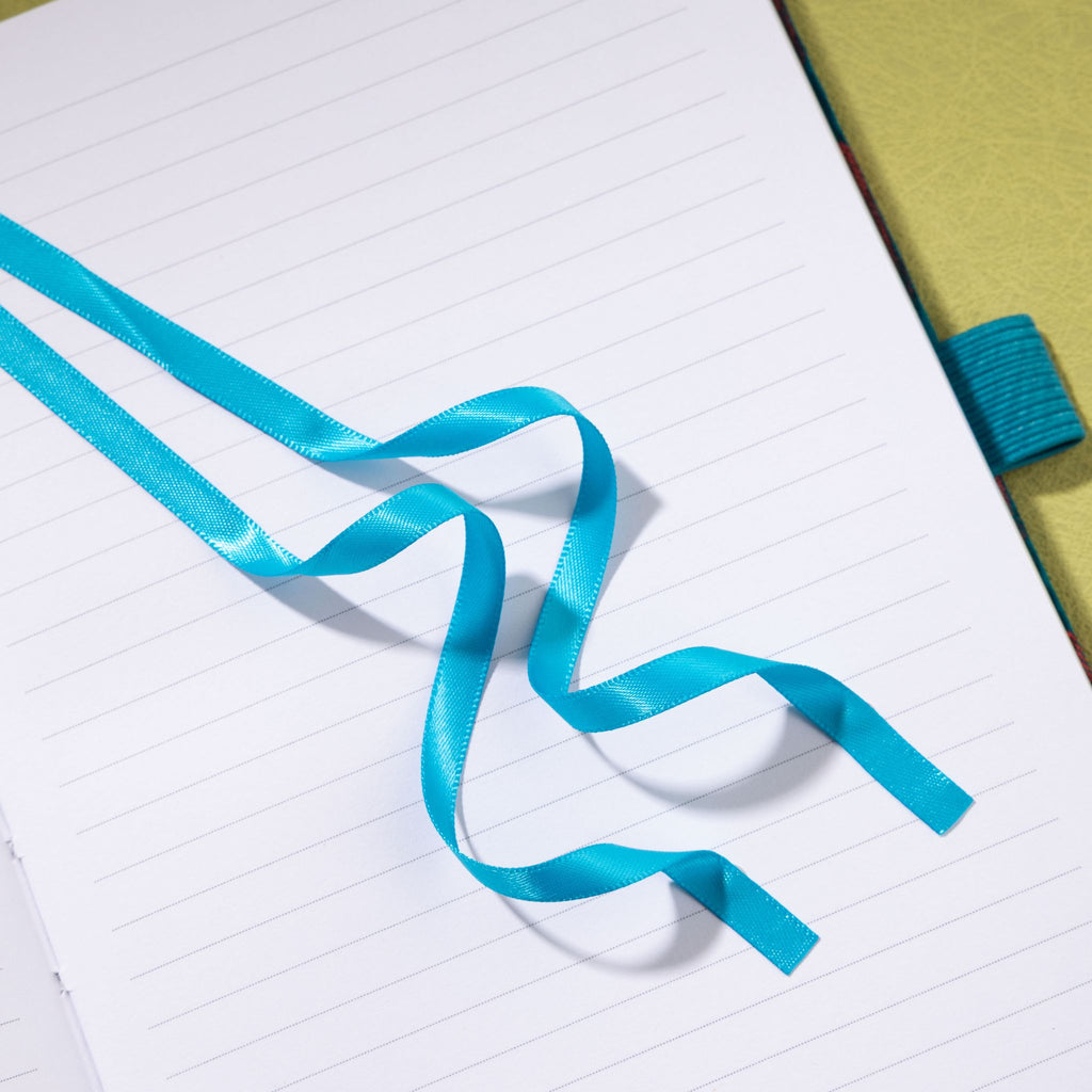 Close-up of the satin ribbon bookmark resting on the lined interior of a teal-blue embroidered journal