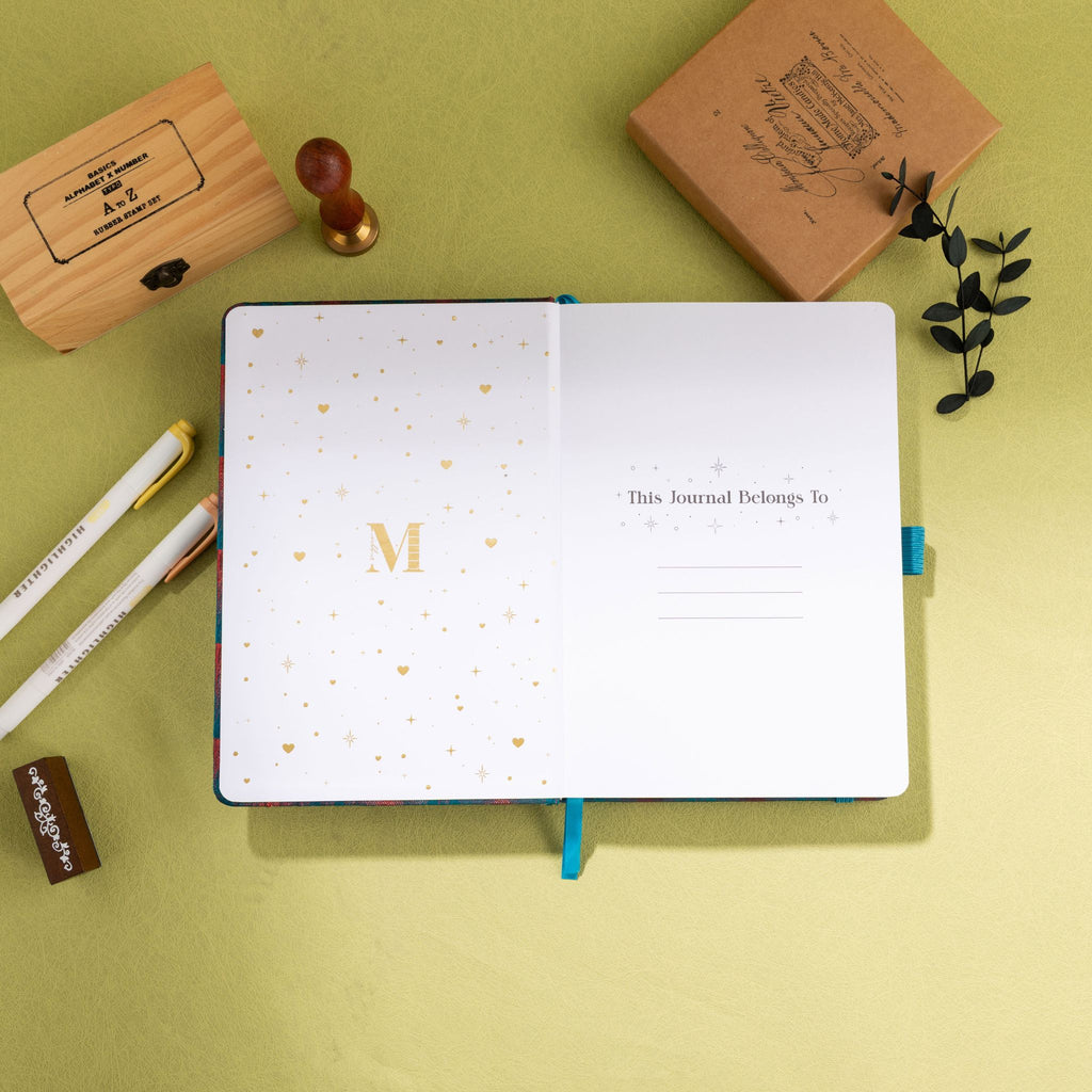 Inside title page featuring a gold foil 'M' logo and 'This Journal Belongs To' section on a teal journal