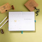 Inside title page featuring a gold foil 'M' logo and 'This Journal Belongs To' section on a teal journal