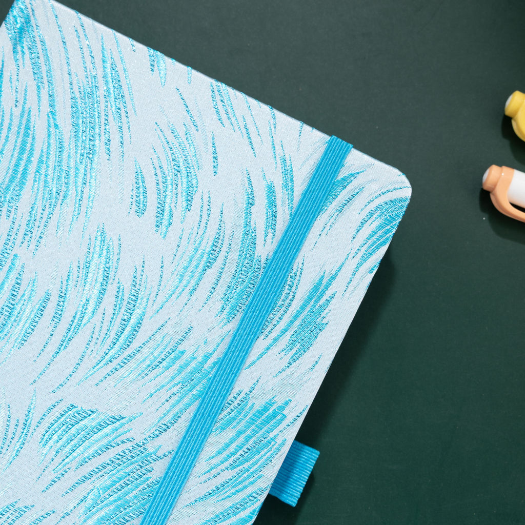 Close-up of the raised light blue embroidery on a white woven fabric cover, with elastic strap