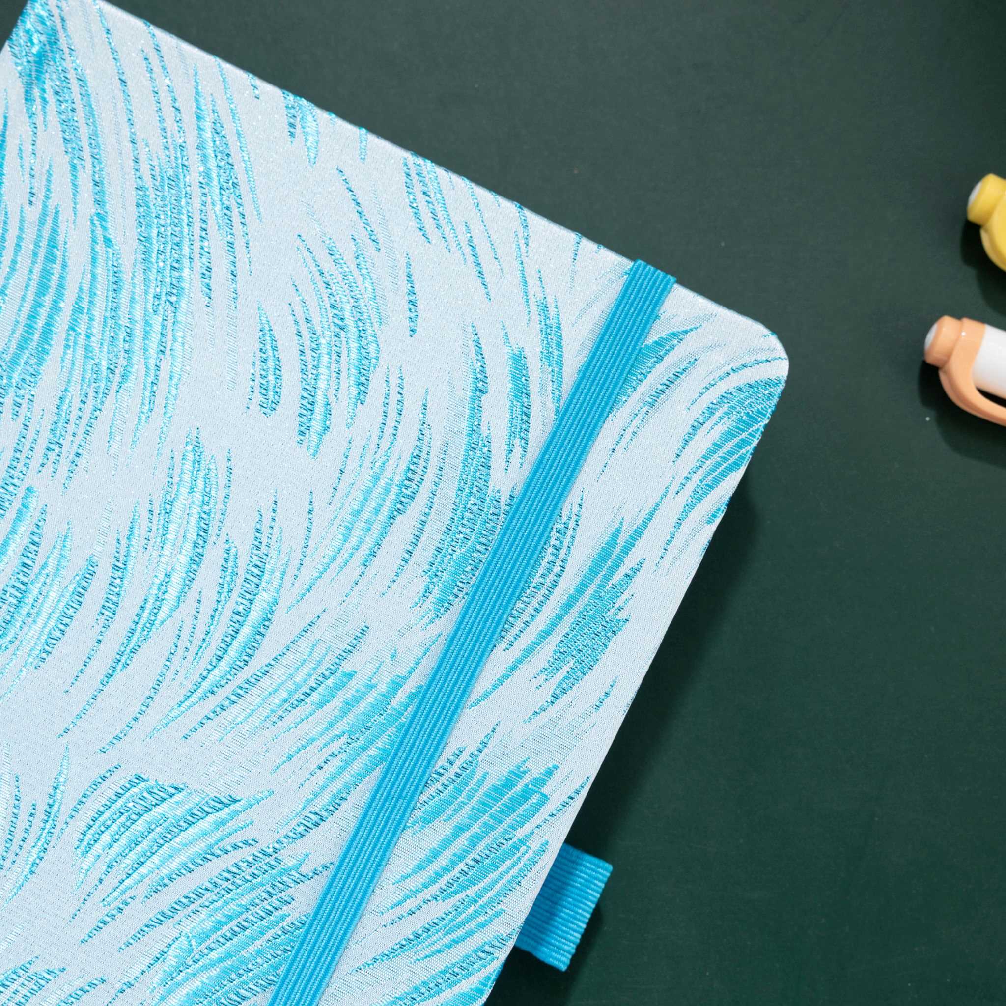 Close-up of the raised light blue embroidery on a white woven fabric cover, with elastic strap