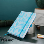 A5 light blue embroidered fabric notebook standing tilted on a dark green desk with candles and pens