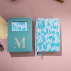 Light blue embroidered feather fabric notebook displayed next to its signature light blue window-cut gift box