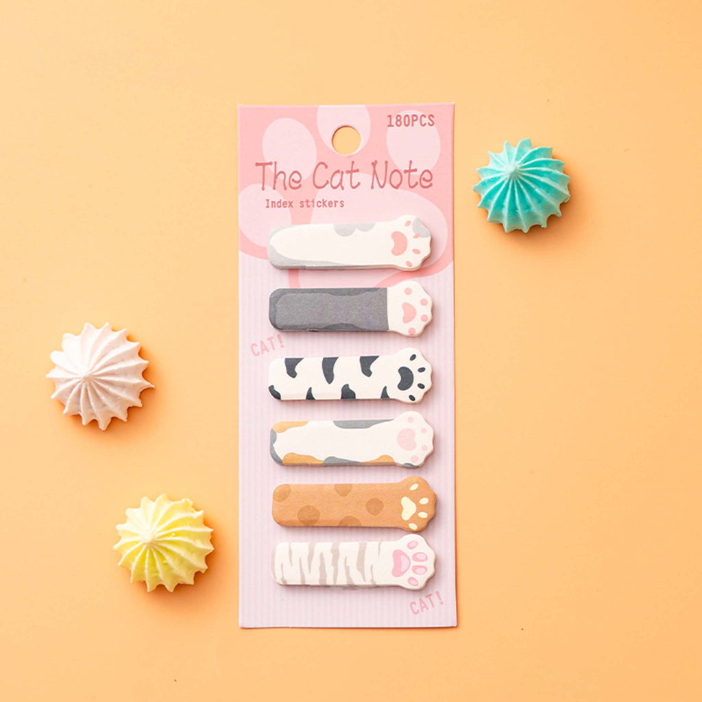 A set of six cat-themed index stickers on a pink backing card, labeled 'The Cat Note' and '180PCS'. The backing card is displayed on a peach-colored background with decorative paper starburst props.