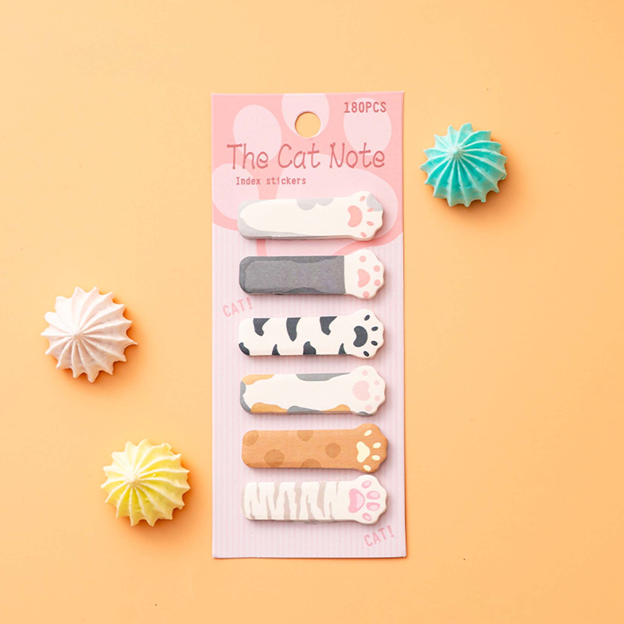 A set of six cat-themed index stickers on a pink backing card, labeled 'The Cat Note' and '180PCS'. The backing card is displayed on a peach-colored background with decorative paper starburst props.