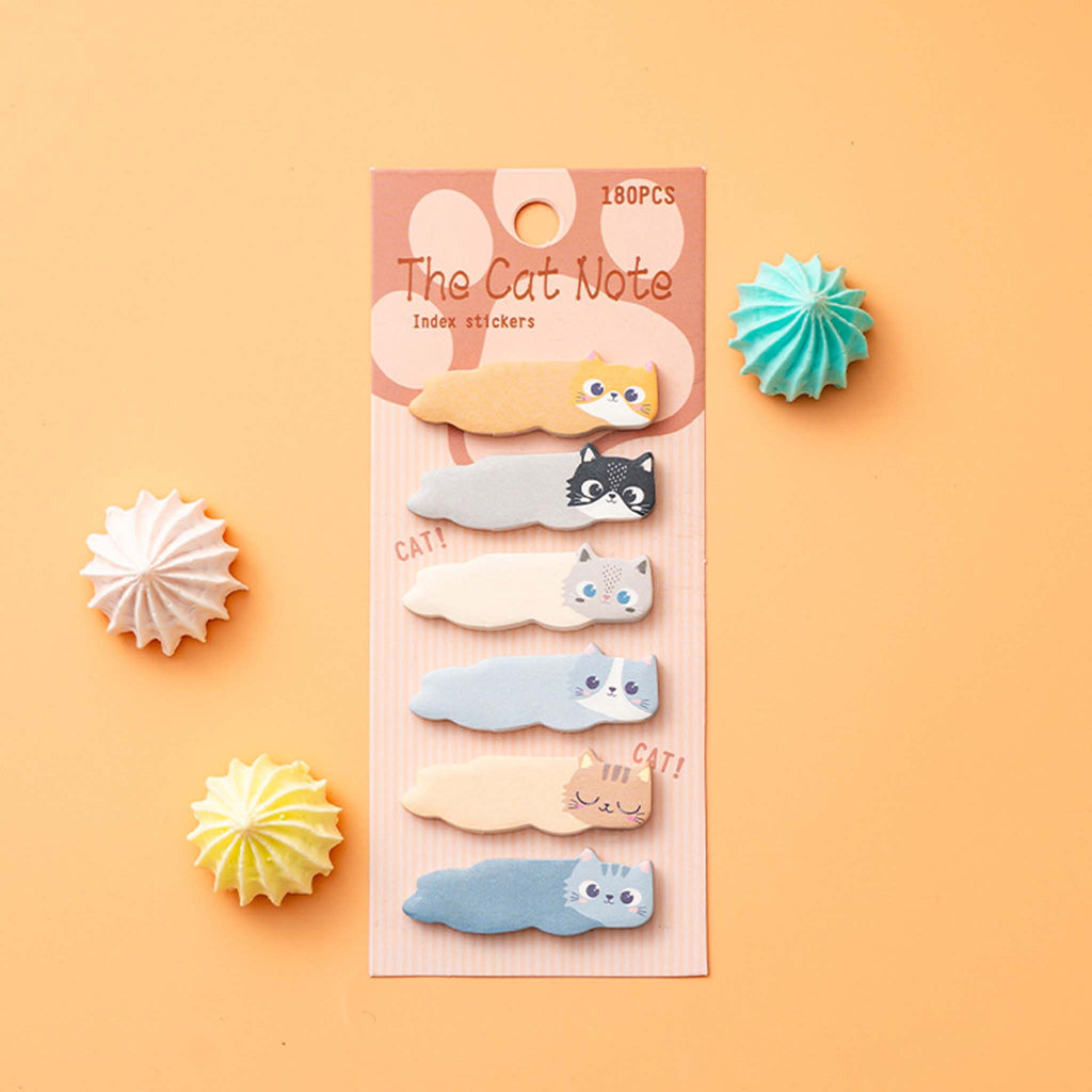 A set of cute cat-shaped sticky notes in various colors, packaged on a pink card labeled 'The Cat Note'. The package is displayed on a peach-colored background with decorative paper starburst props.