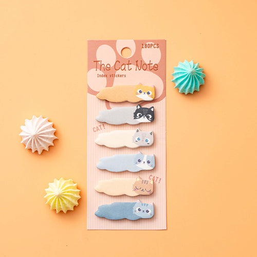 A set of cute cat-shaped sticky notes in various colors, packaged on a pink card labeled 'The Cat Note'. The package is displayed on a peach-colored background with decorative paper starburst props.