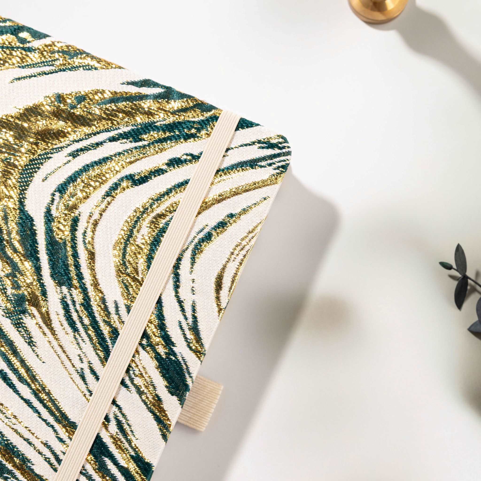 Close-up of the woven dark green fabric cover with shimmering gold marble lines and elastic strap.