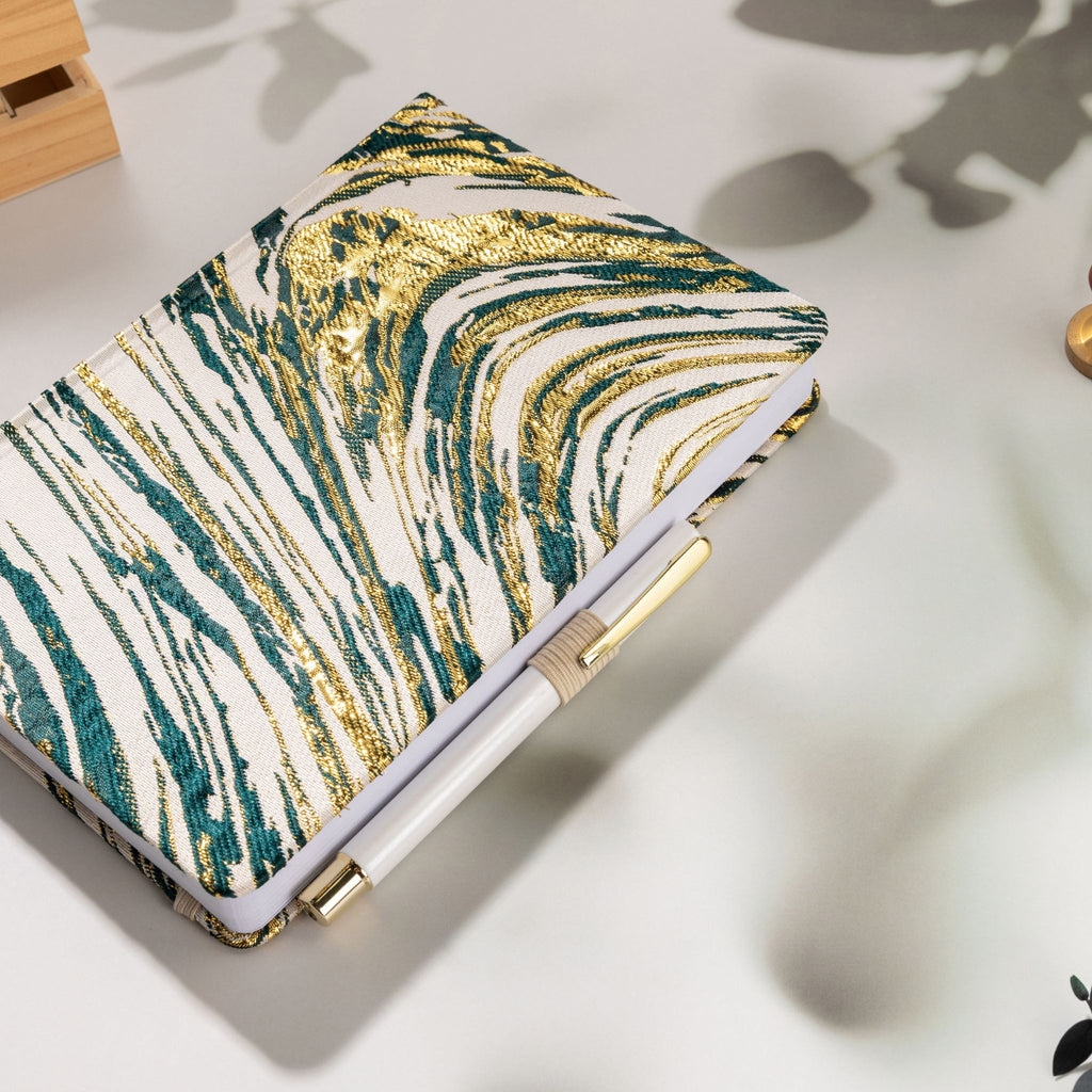 Deep green and gold swirl fabric notebook with elastic band, holding a white and gold pen