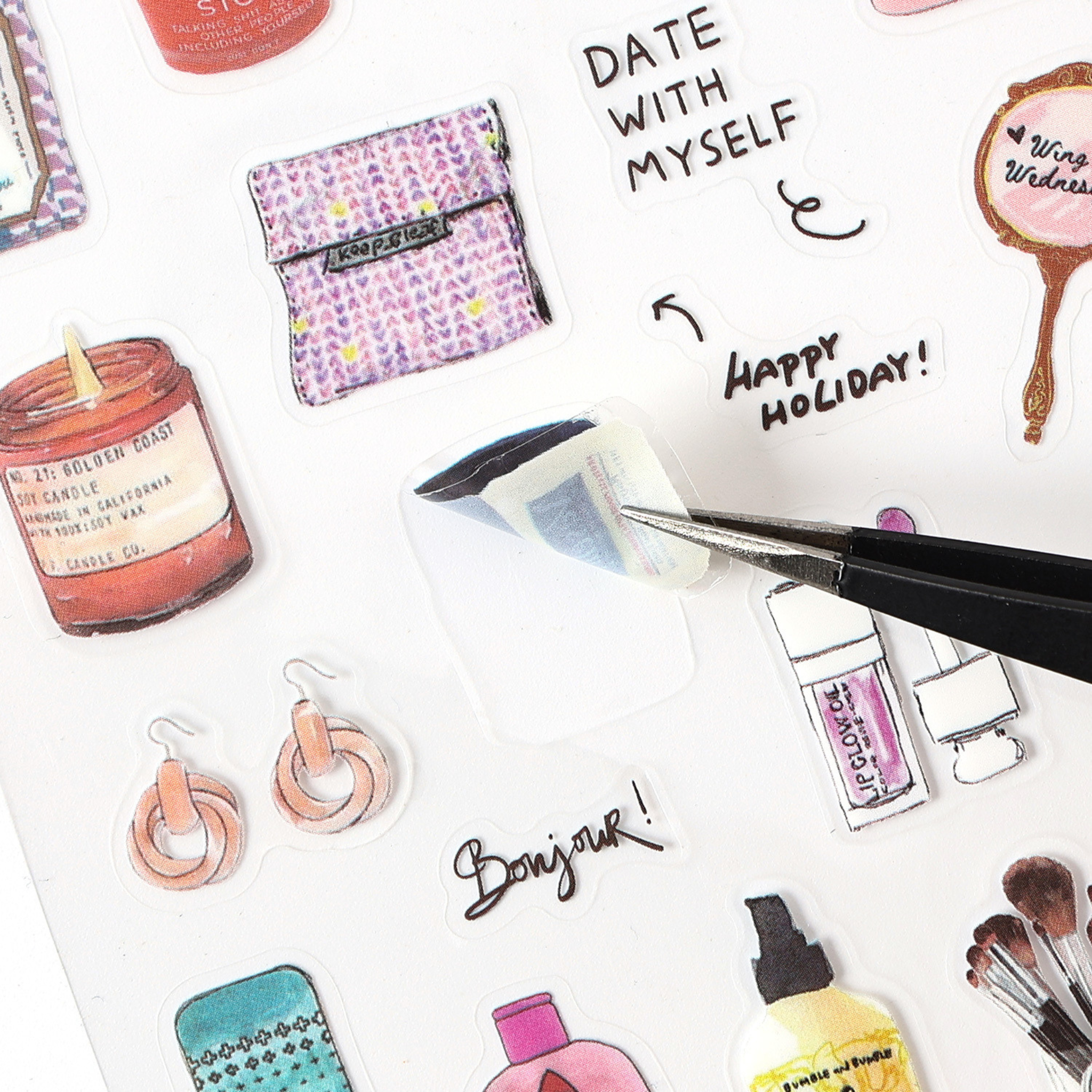 A close-up of a watercolor PET sticker being peeled off its backing using black tweezers, surrounded by illustrated items including a scented candle, a pouch, earrings, lip gloss, and a hand mirror, with handwritten phrases like "DATE WITH MYSELF" and "HAPPY HOLIDAY!".