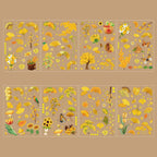 Eight sheets of Ginkgo Song gold foil PET stickers displayed on a warm brown background, featuring golden ginkgo leaves, sunflowers, birds, persimmons, butterflies, and tiny sparkling stars scattered across the designs.