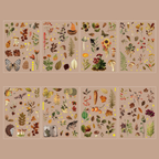 Eight sheets of Autumn Song gold foil PET stickers displayed on a warm beige background, featuring fall-themed botanical elements such as acorns, pinecones, dried leaves, mushrooms, berries, sunflowers, butterflies, and a small hedgehog.