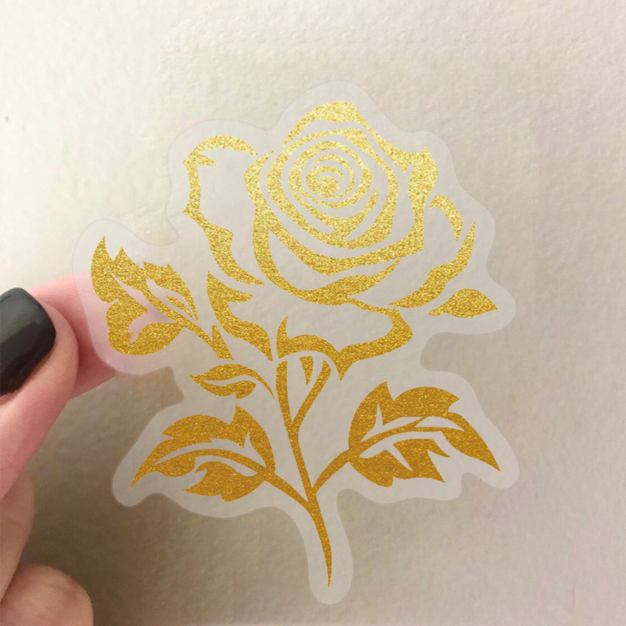 A close-up of a gold foil rose PET sticker being held by a hand, with a translucent border and detailed gold foil petals.