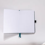 Open A5 journal showing the 160gsm dot grid interior pages with teal ribbon bookmark