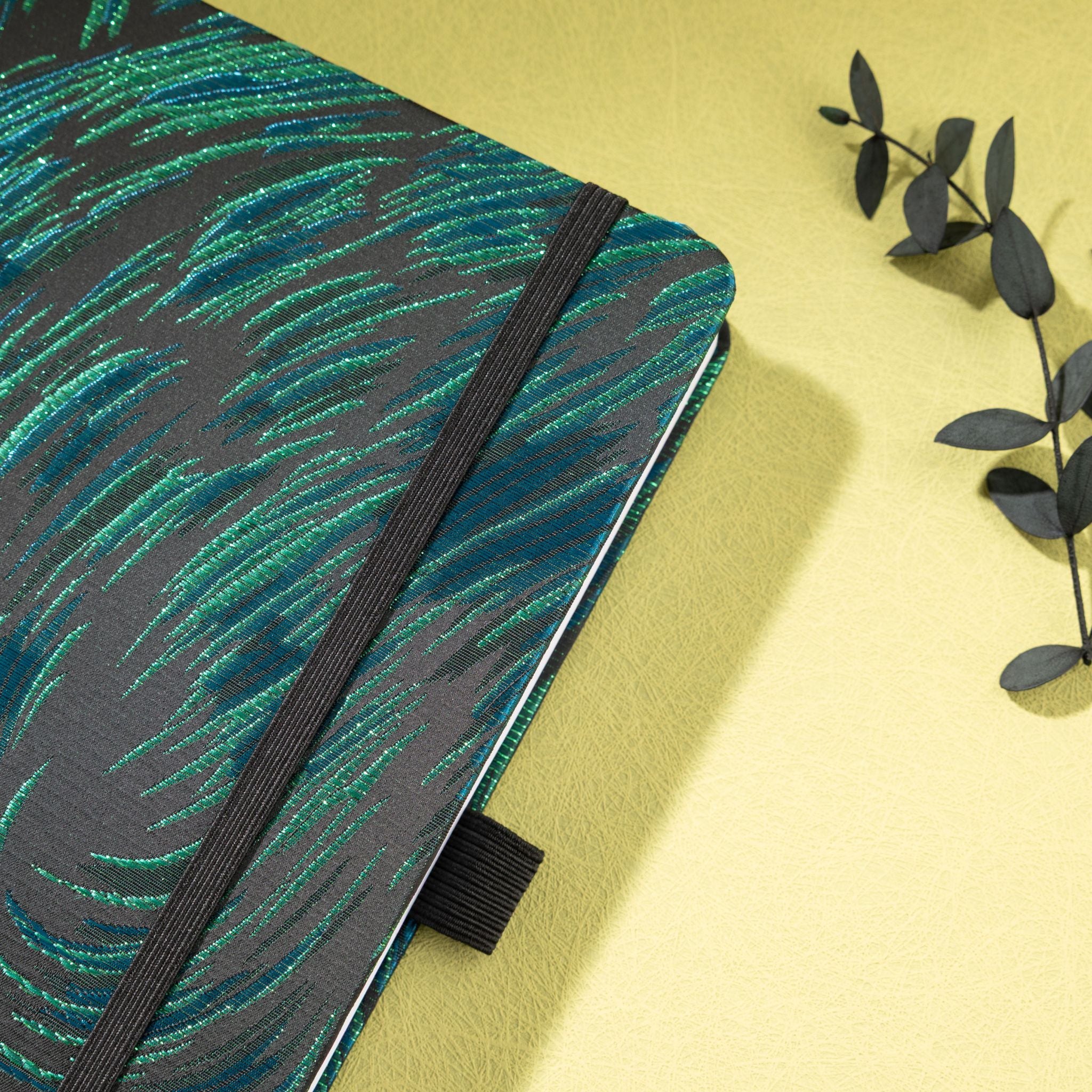 Close-up of the raised green embroidered texture on a black woven fabric cover, with elastic strap