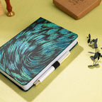 Black and green embroidered fabric notebook with elastic band, holding a white and gold pen