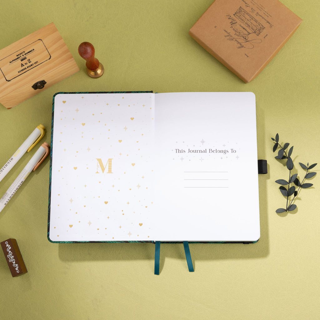 Inside title page featuring a gold foil 'M' logo and 'This Journal Belongs To' section on a green embroidered journal