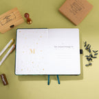 Inside title page featuring a gold foil 'M' logo and 'This Journal Belongs To' section on a green embroidered journal