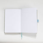 Open A5 journal showing the thick 160gsm dot grid interior pages and light blue ribbon bookmark