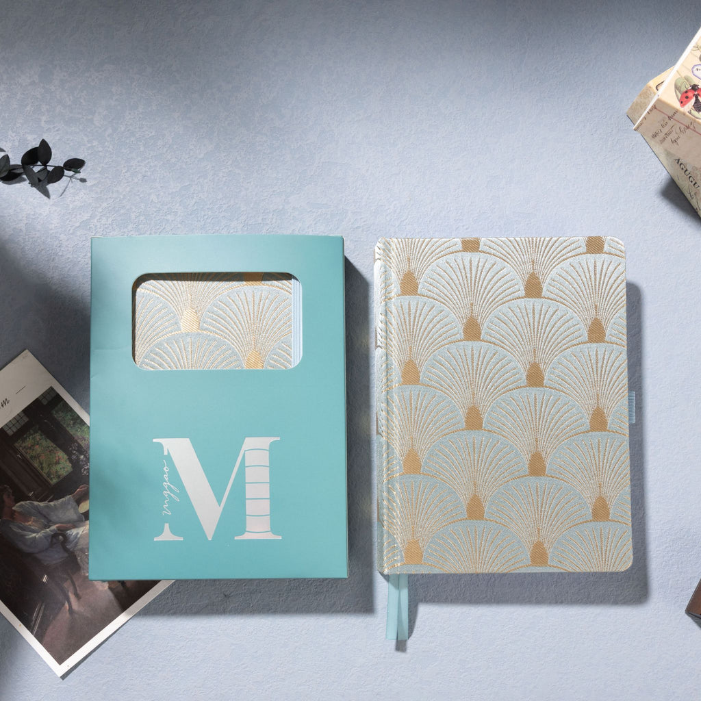 Green scalloped fabric notebook placed next to its signature light blue window-cut gift box