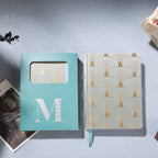 Green scalloped fabric notebook placed next to its signature light blue window-cut gift box