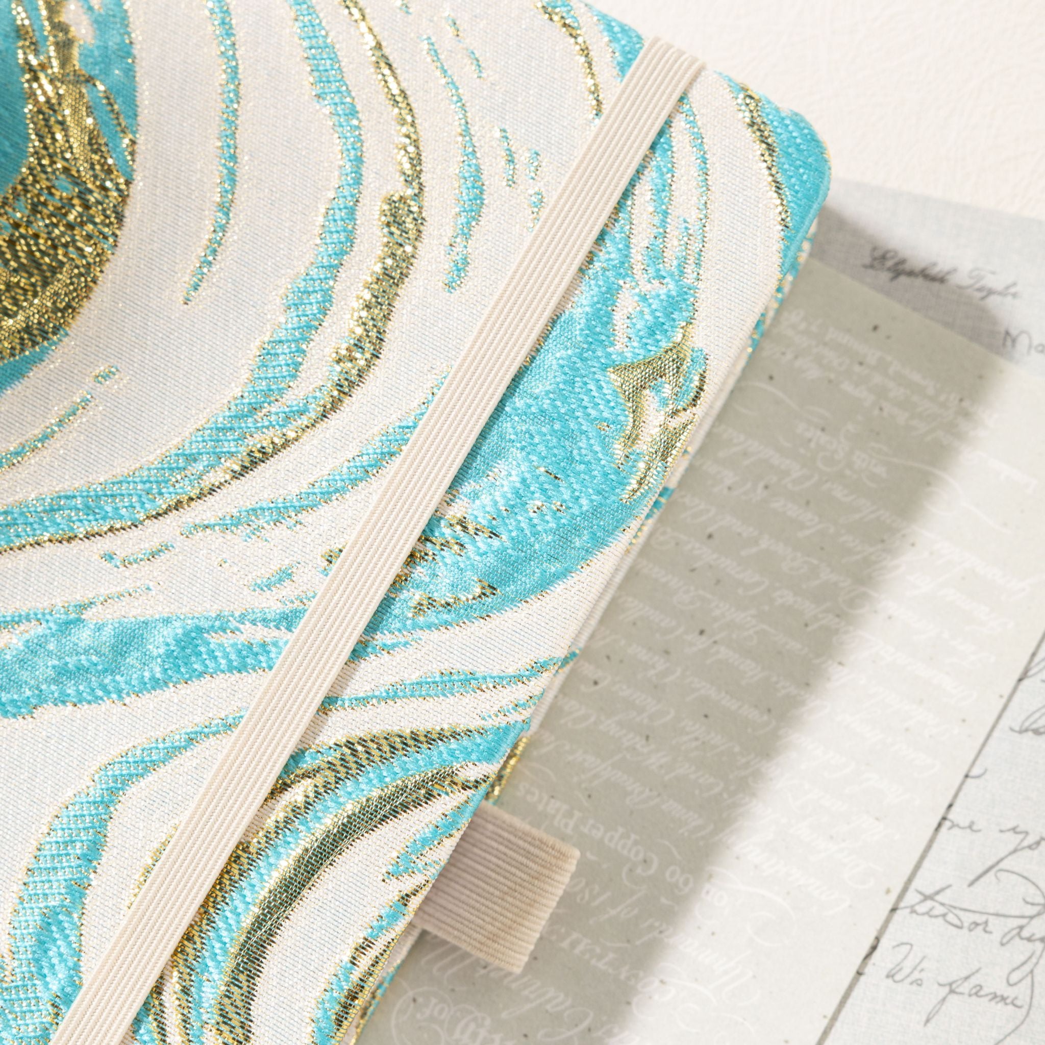 Close-up of the textured woven cloth cover featuring teal and metallic gold marble swirls with elastic band
