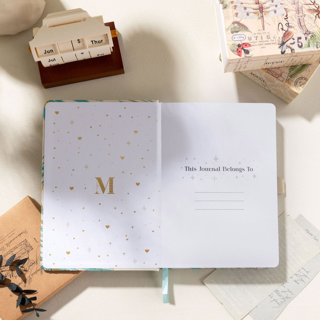 Inside opening page featuring gold foil "M" logo and "This Journal Belongs To" ownership section with heart and star decorations