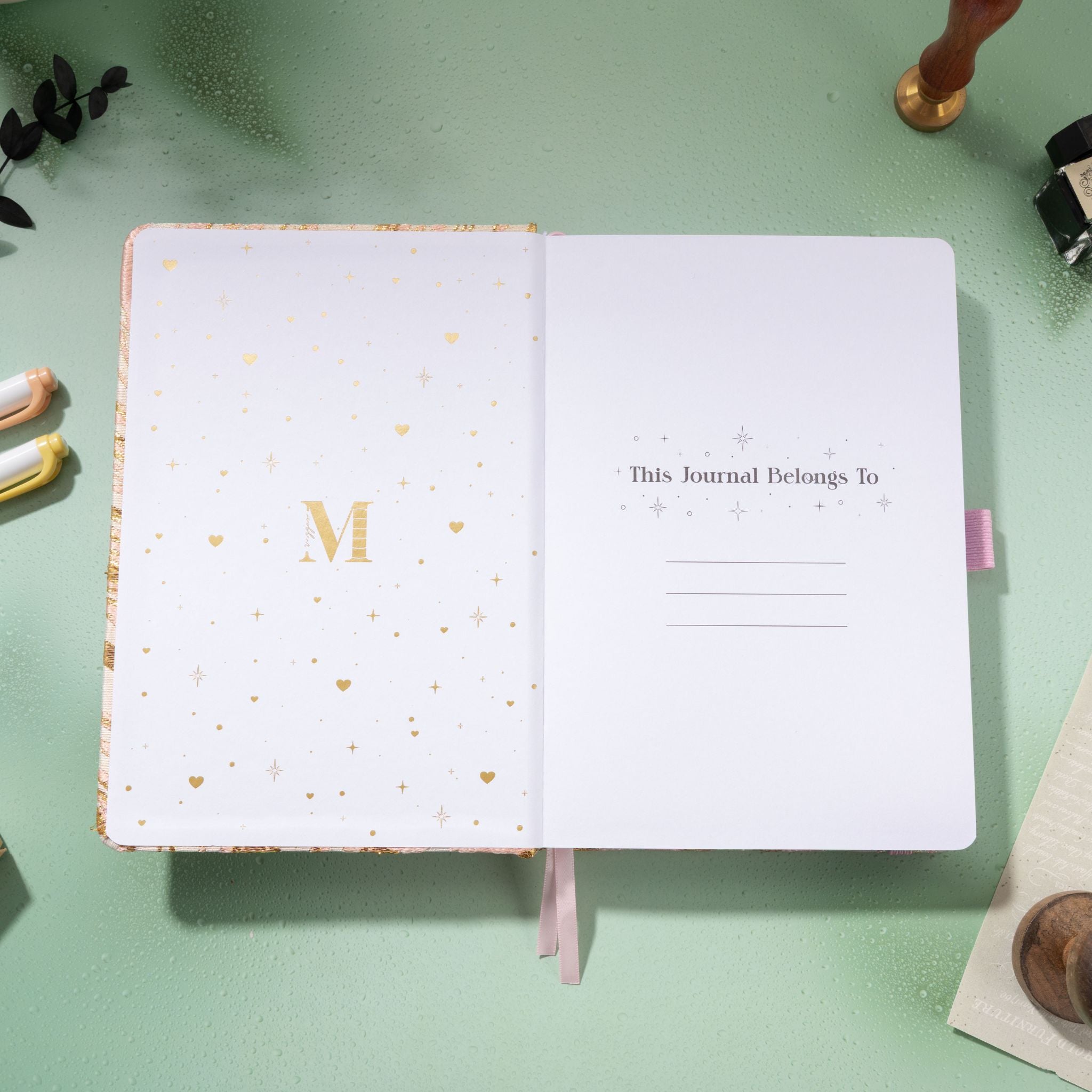 Inside title page featuring gold foil 'M' logo and 'This Journal Belongs To' section on a pink journal
