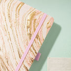 Close-up of the woven pink fabric cover with swirling gold marble lines and matching elastic strap