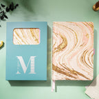 Pink and gold marble fabric notebook displayed next to its signature light blue window-cut gift box