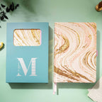 Pink and gold marble fabric notebook displayed next to its signature light blue window-cut gift box