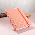 A5 red scalloped fabric journal tilted on a white surface, showing the hardcover thickness and side edge