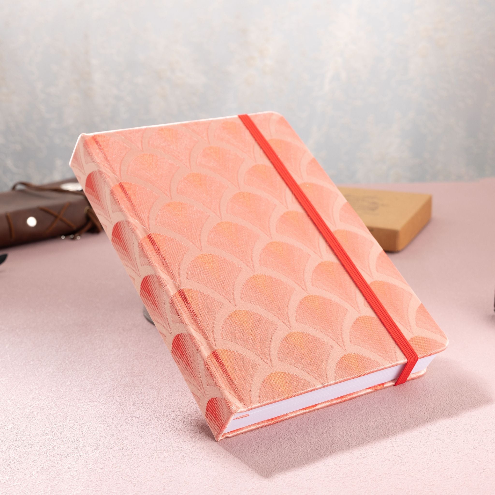 A5 red scalloped fabric journal tilted on a white surface, showing the hardcover thickness and side edge