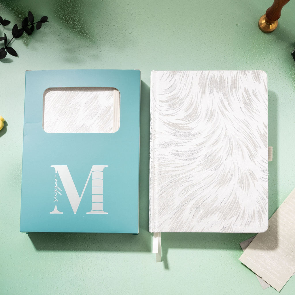 White and silver embroidered fabric notebook displayed next to its signature light blue window-cut gift box