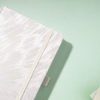 Close-up of the raised silver embroidered texture on a white fabric cover, with elastic strap