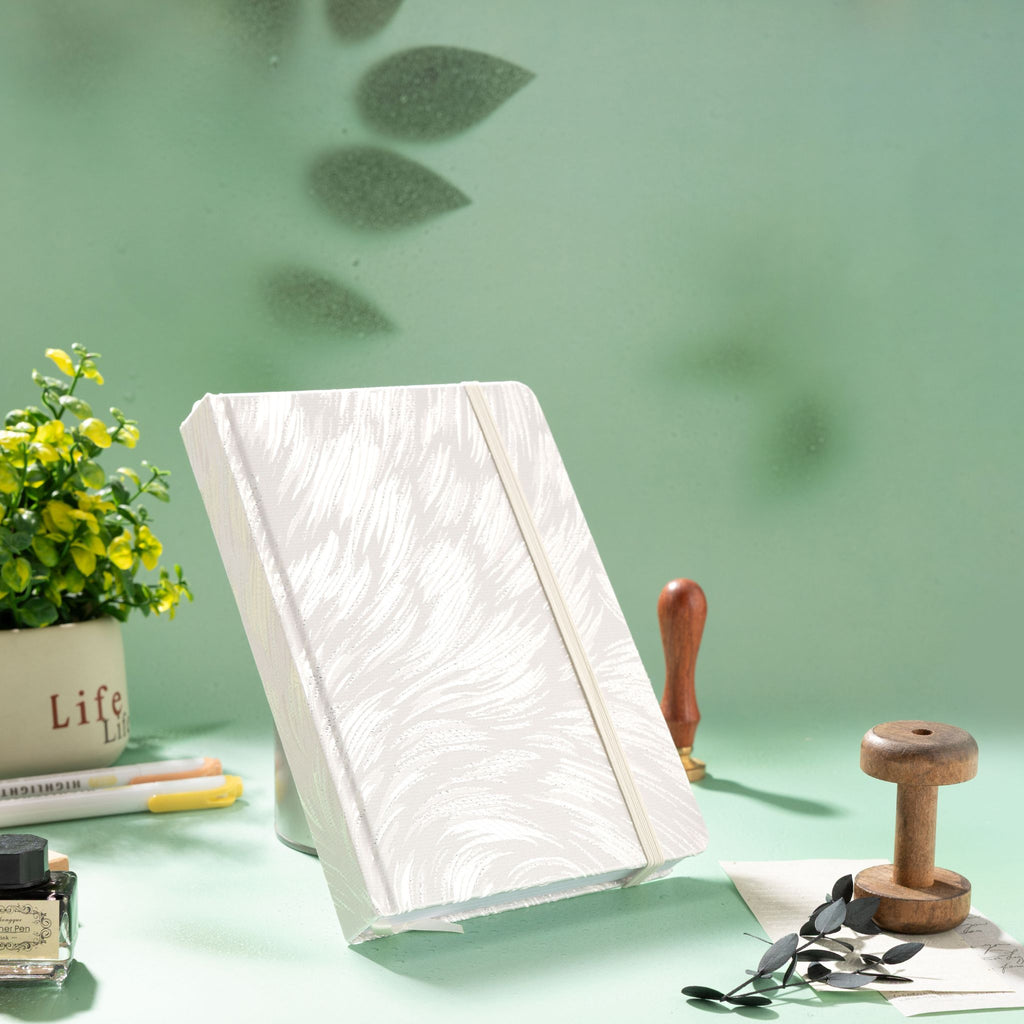 A5 white and silver embroidered fabric notebook standing upright on a green desk with a wax seal stamp