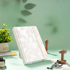 A5 white and silver embroidered fabric notebook standing upright on a green desk with a wax seal stamp