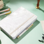 White and silver embroidered fabric notebook with elastic band, holding a white and gold pen