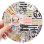 A hand holds a circular collage of vintage-style paper stickers and text decals in assorted colors, including beige, pink, blue, black, and white, on a plain white background.