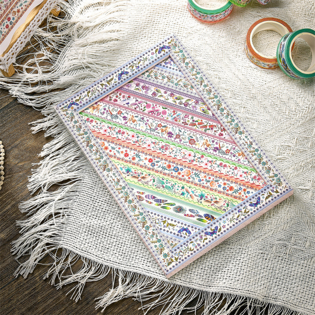 A notebook page decorated with rows of vintage floral and bird washi tapes, laid flat on a white fringed fabric, showing how the tapes look in journaling projects.