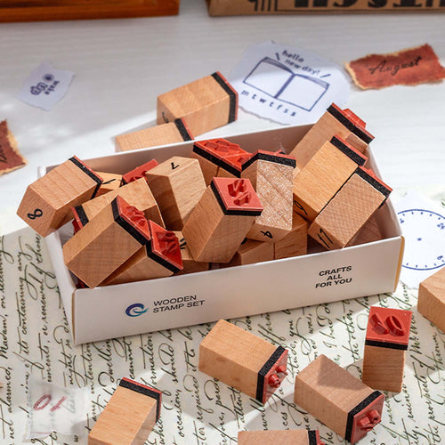 Wooden number stamps scattered on a white desk with vintage handwritten paper, showing the stamps outside their white storage box in a creative journaling setup.