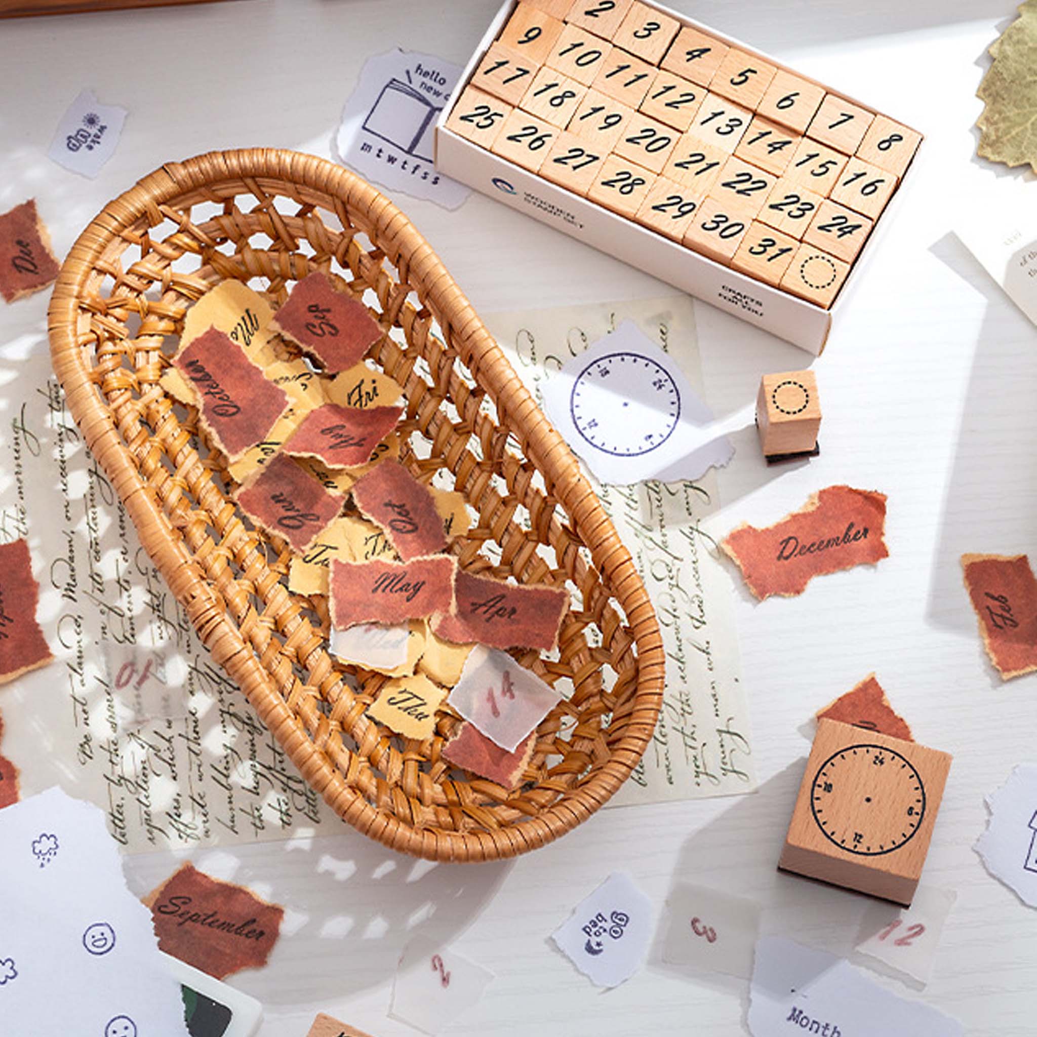 A woven rattan basket filled with stamped paper cutouts and loose wooden number stamps, styled on a desk with vintage script paper for a warm, nostalgic journaling aesthetic.