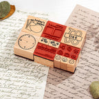 A close-up of wooden daily planner stamps with visible red rubber stamping surfaces, arranged on vintage handwritten paper with dried leaves, showcasing the stamp carving details and natural wood texture.