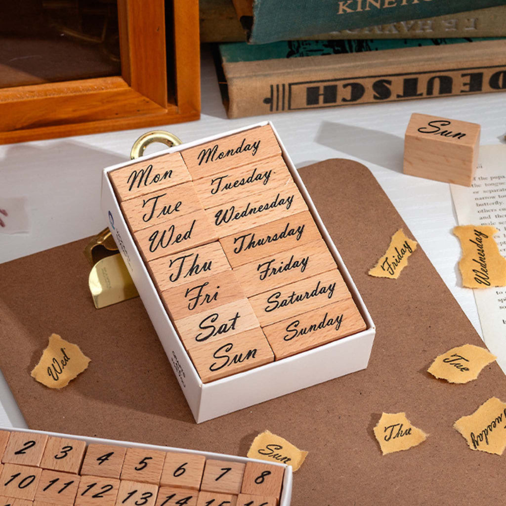 A white storage box containing 14 wooden weekday stamps, featuring both full and abbreviated forms of Monday through Sunday, arranged in a 2×7 grid on a white background.