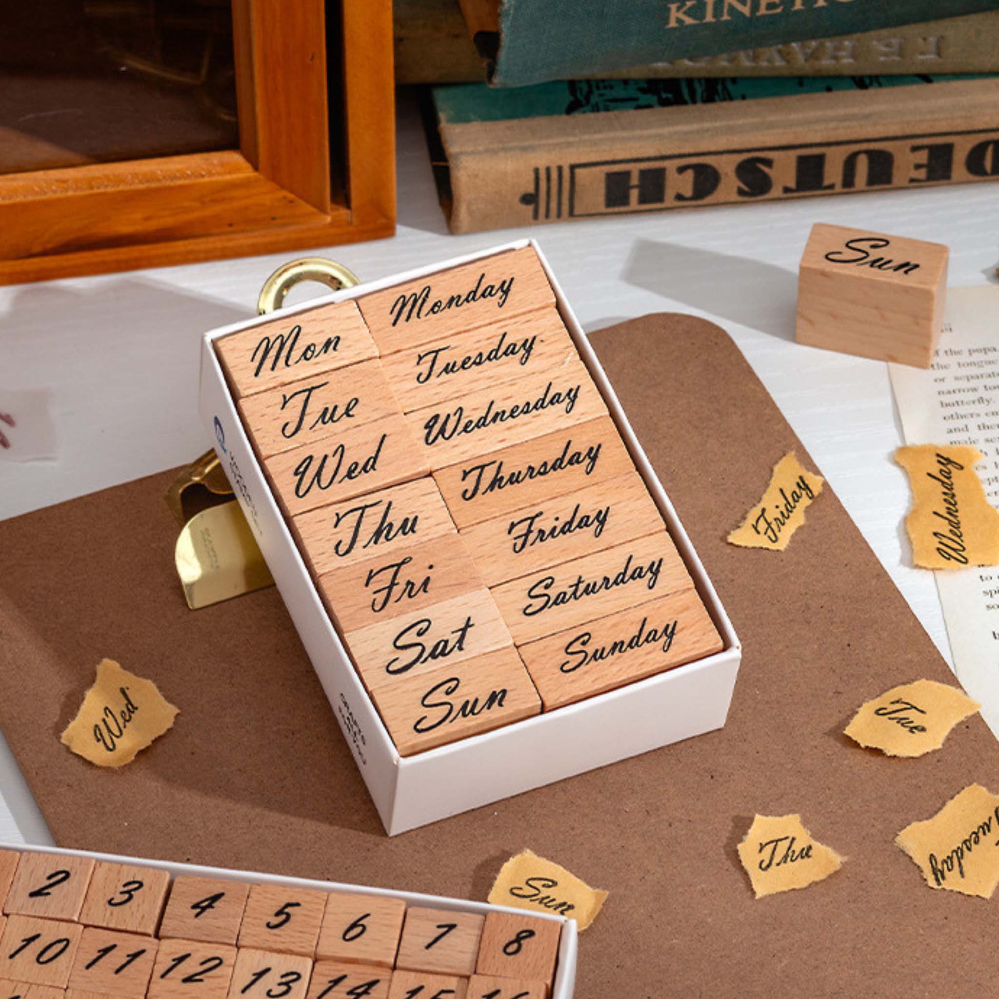 A white storage box containing 14 wooden weekday stamps, featuring both full and abbreviated forms of Monday through Sunday, arranged in a 2×7 grid on a white background.